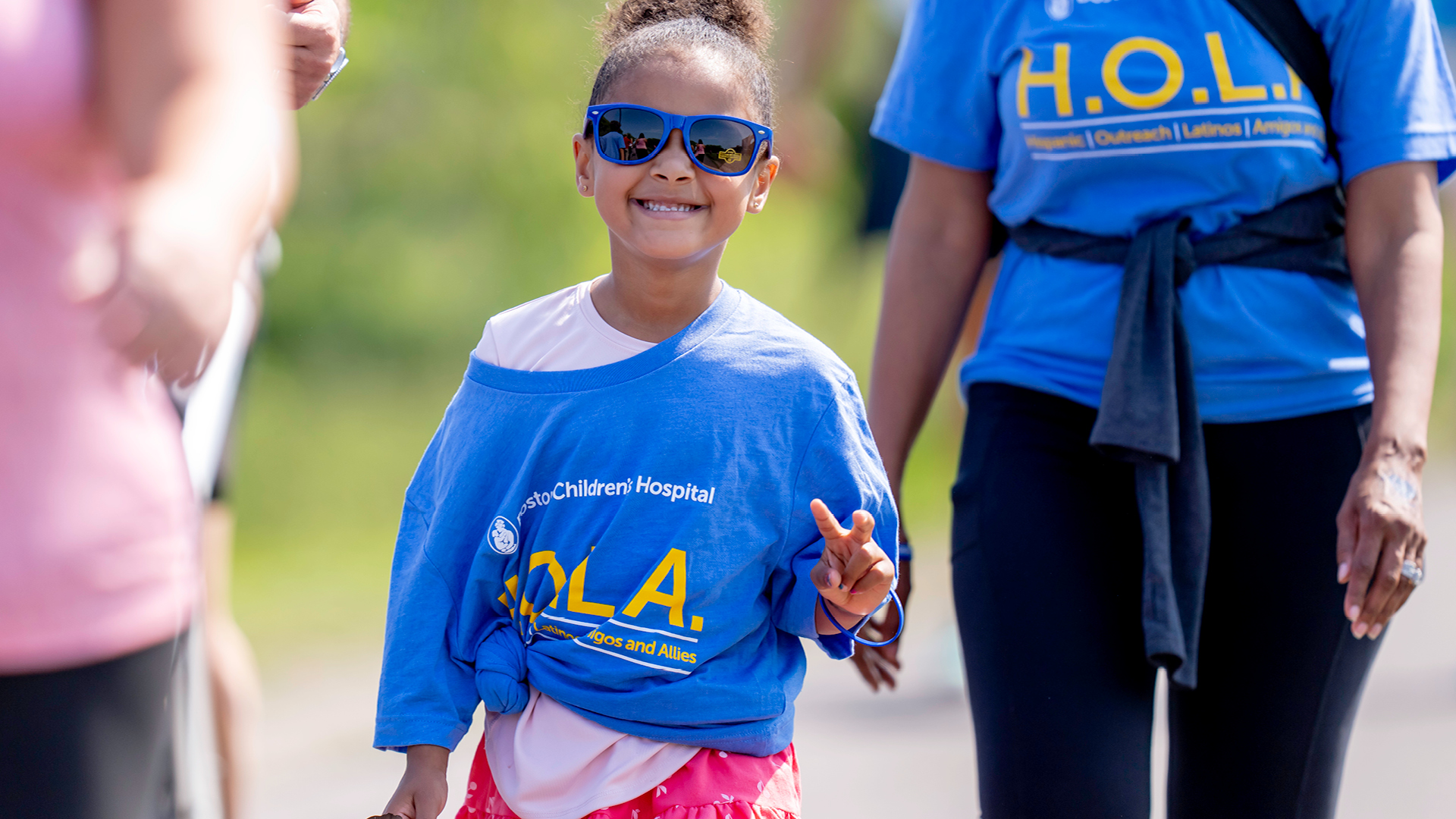 A young girl wearing sunglasses walks next to her mom at the Eversource Walk for Kids