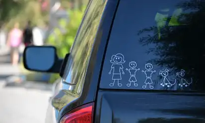 The back windshield of a car that has a set of stickers of a pencil figure family