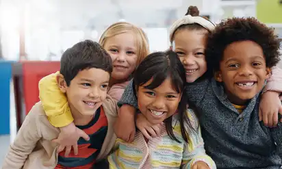 A group of five children smiling and hugging each other