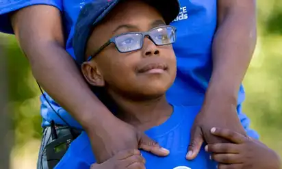 A young boy, Malembo, stands in front of his parent and holds their hands