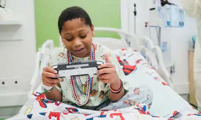 A young boy sits in a hospital bed plying a handheld gaming console