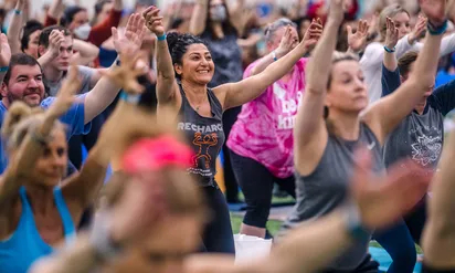 A large group of Yoga Reaches Out event participants raise their arms to the sky