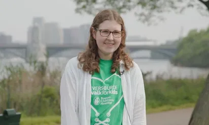 girl with glasses in green shirt standing along the Charles River in Boston