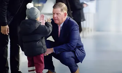 Man in blue suit squatting to high five a child with winter coat and hat