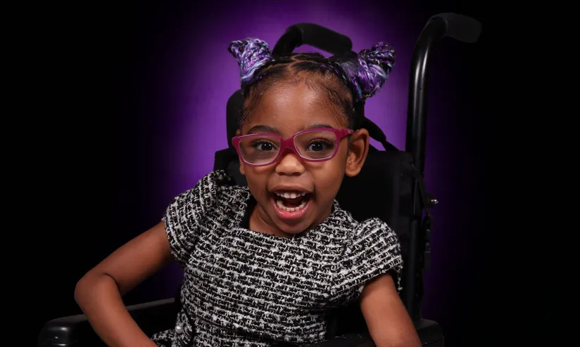 young girl smiling in pink glasses on a wheelchair