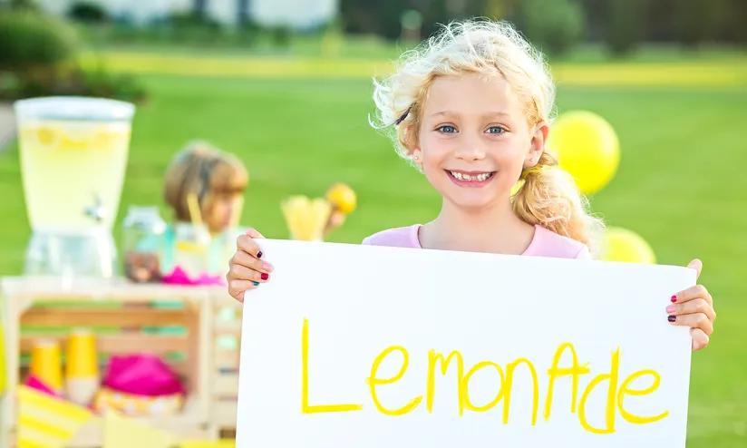 girl holding up poster with the word lemonade on it