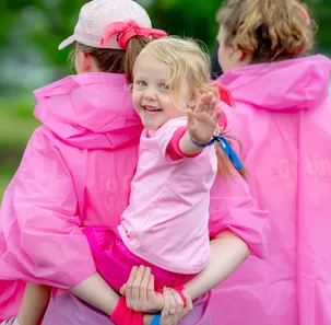 Two women in pink jackets and a little girl waving and smiling in a pink t-shirt.