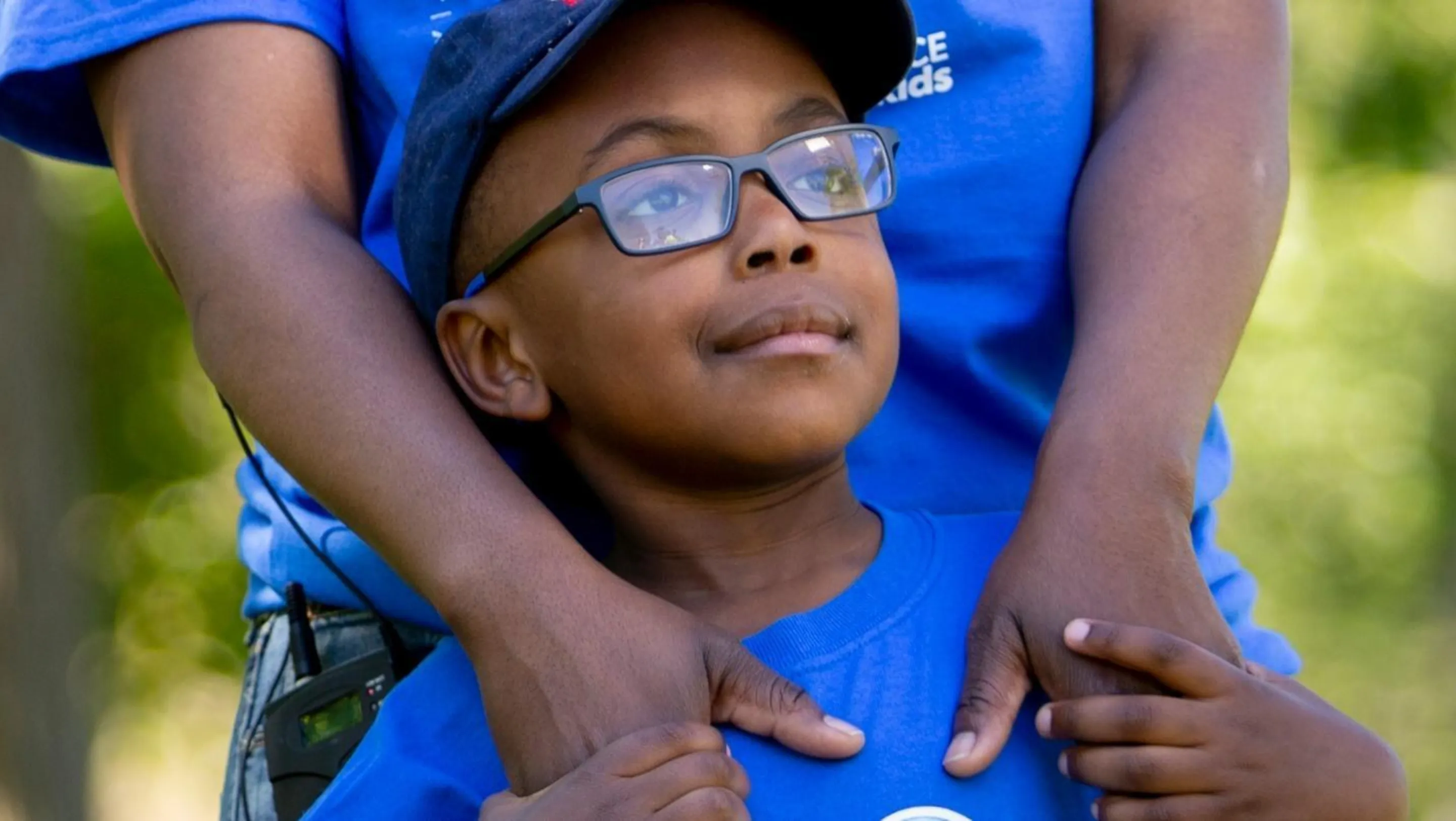 A young boy, Malembo, stands in front of his parent and holds their hands