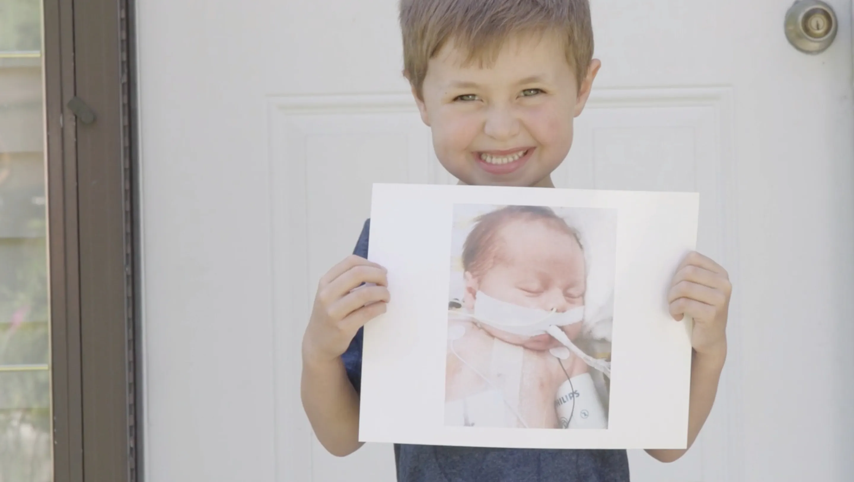 A young patient, Presley, grins while holding a photo of himself as a baby when he was undergoing treatment at BCH