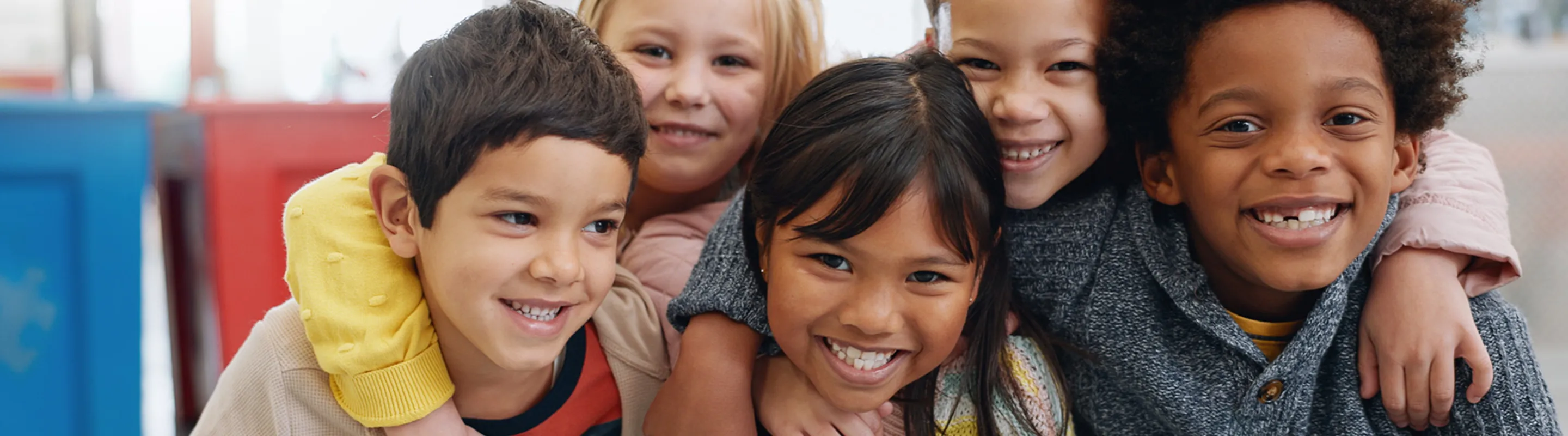A group of five children smiling and hugging each other
