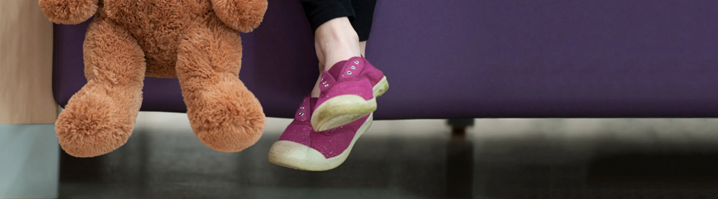 child's feet crossed sitting on a purple sofa with teddy bear