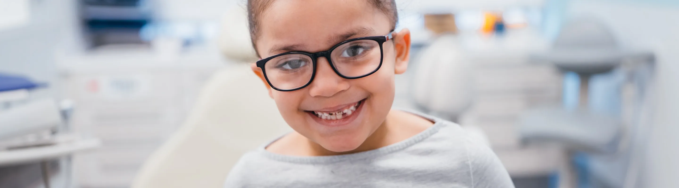young girl with ponytail and glasses smiling in hospital room
