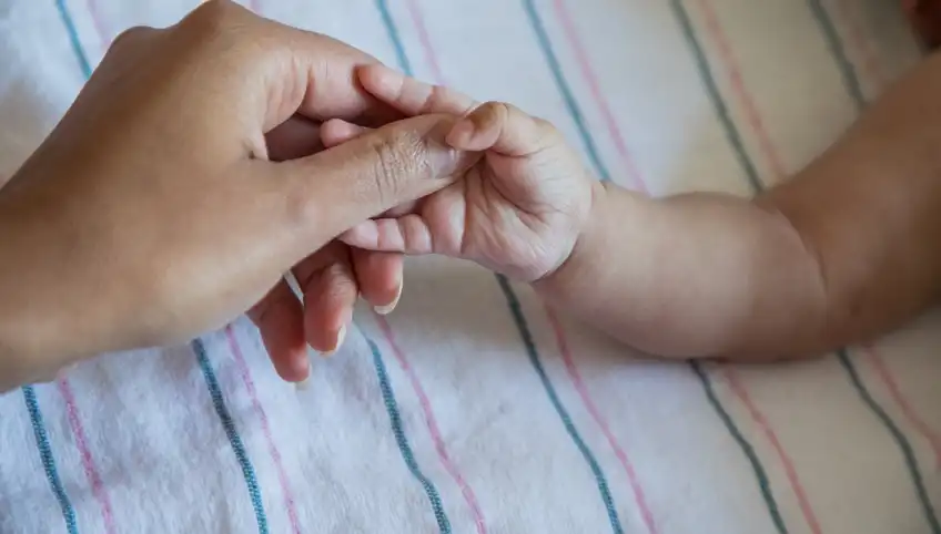 A closeup shot of an adult hand holding a small baby's hand