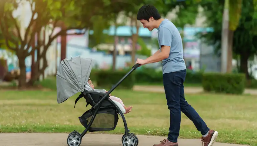 A man walking in a park pushing a baby stroller