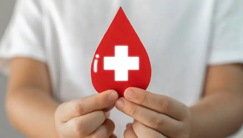 A closeup shot of hands holding a blood droplet with a white medical cross in the center