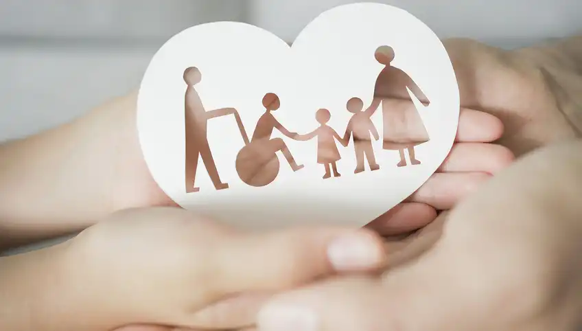 A closeup of two sets of hands holding a paper cutout of a family in the shape of a heart