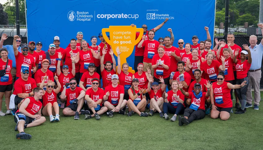A large group of corporate cup participants wearing matching orange shirts pose at the awards ceremony