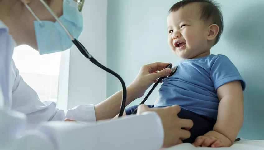 A baby laughs as a doctor listens to his heart with a stethoscope