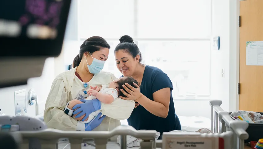 A doctor and nurse look adoringly at a small baby patient who is being cradled in the doctor's arms