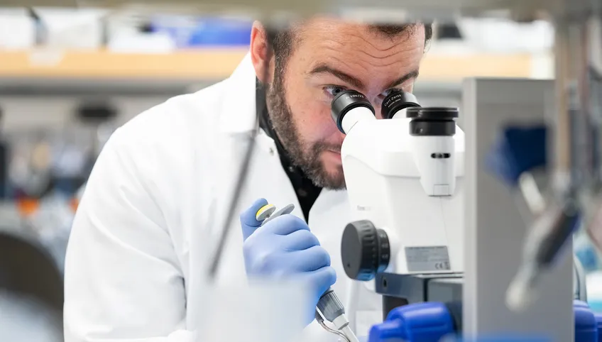 Boston Children's Hospital research scientist holding pipette peering into microscope