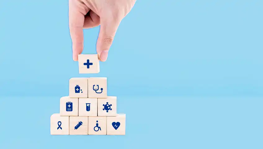 A hand stacks small cubes printed with hospital-related icons