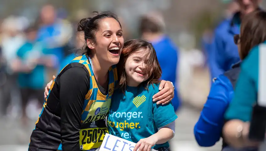 A runner in the Boston Marathon hugs a child wearing a BCHT t-shirt