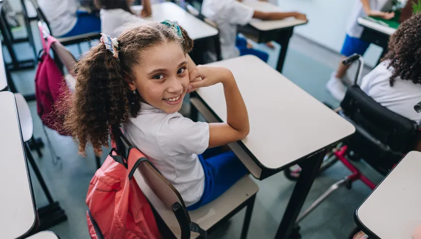 girl smiling looking over her shoulder sitting at a desk in a school