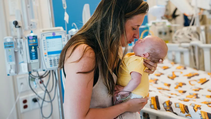 Mother holding baby patient in her arms surrounded by medical equipment in hospital room