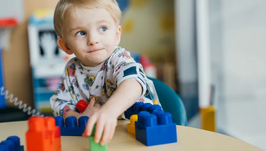 little boy smiling in pajama top playing with Lego-like blocks