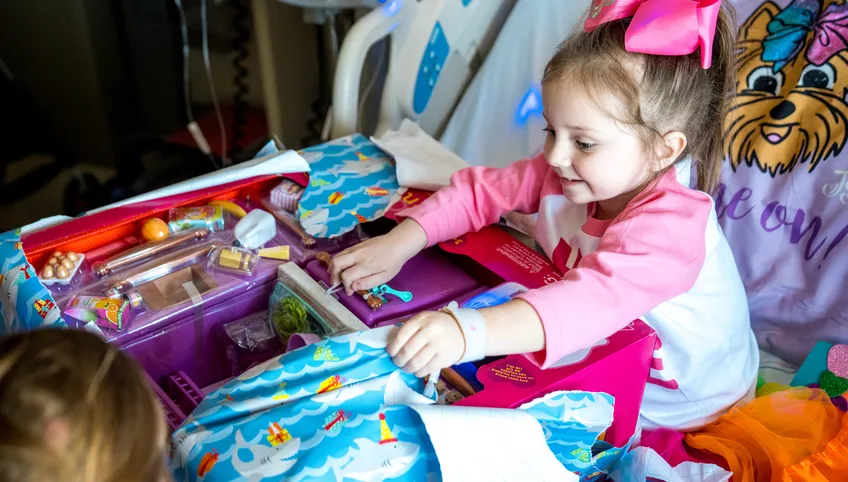 a child wearing a pink and white shirt with long hair and a pink bow plays with colorful toys