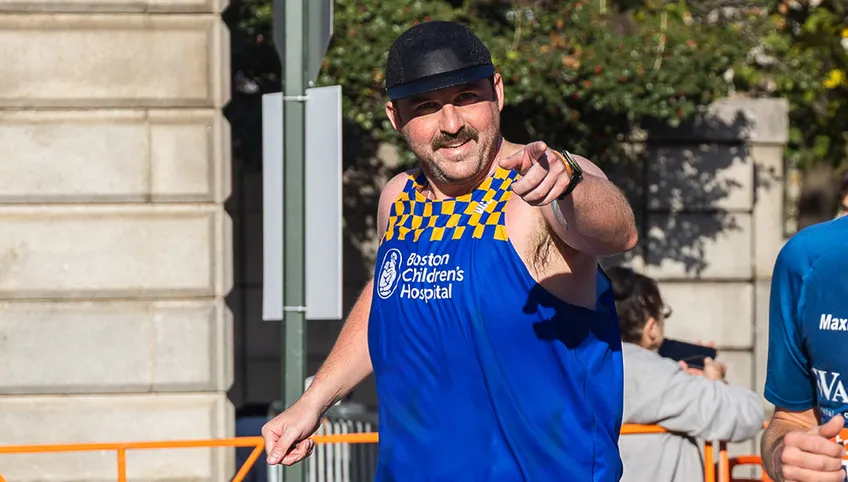 Man with mustache smiling and pointing at camera.