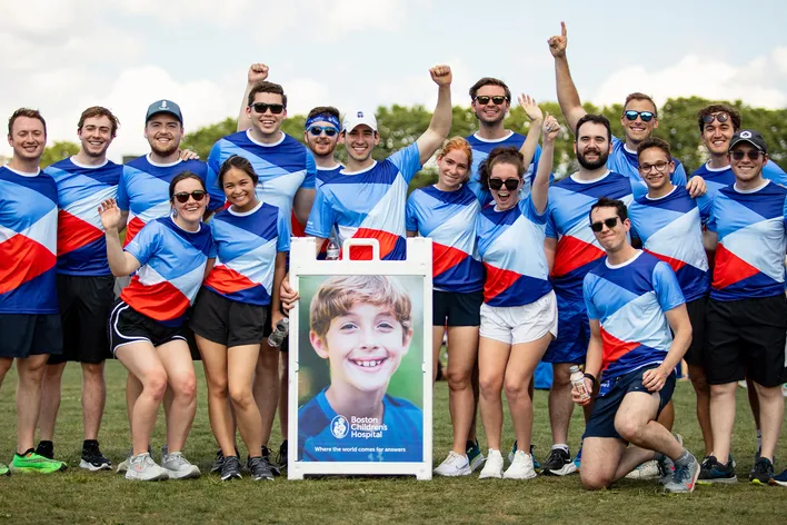 A large group of people wearing matching shirts pose together with a photo of a Boston Children's patient