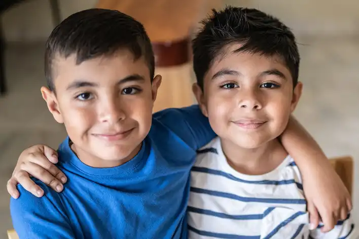 Two boys with their arms around each other smile at the camera