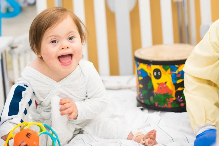 A young baby with Down's syndrome smiling happily at the camera