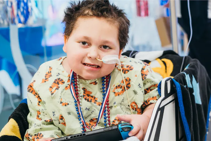boy smiling with breathing tube holding a video game