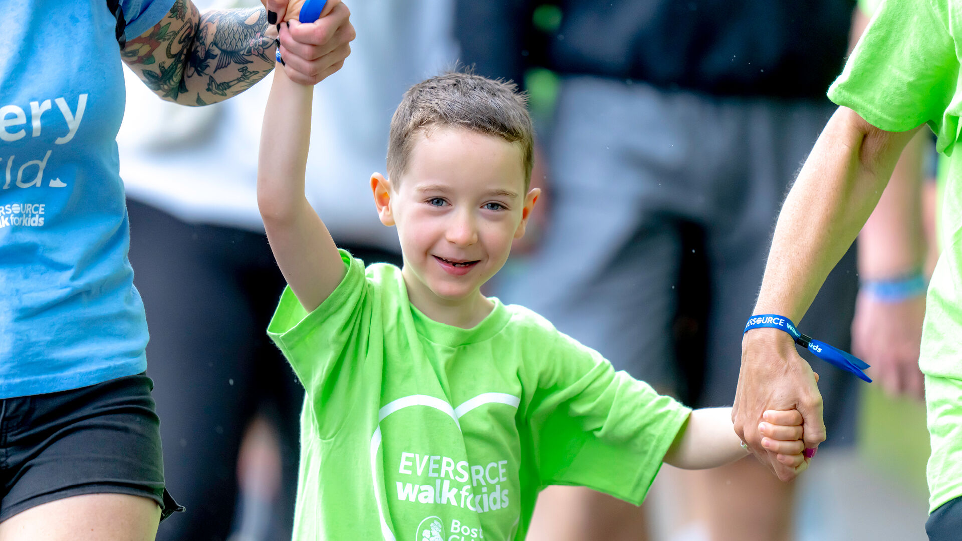 A young, smiling boy holds his parents' hands at the Eversource Walk for Kids