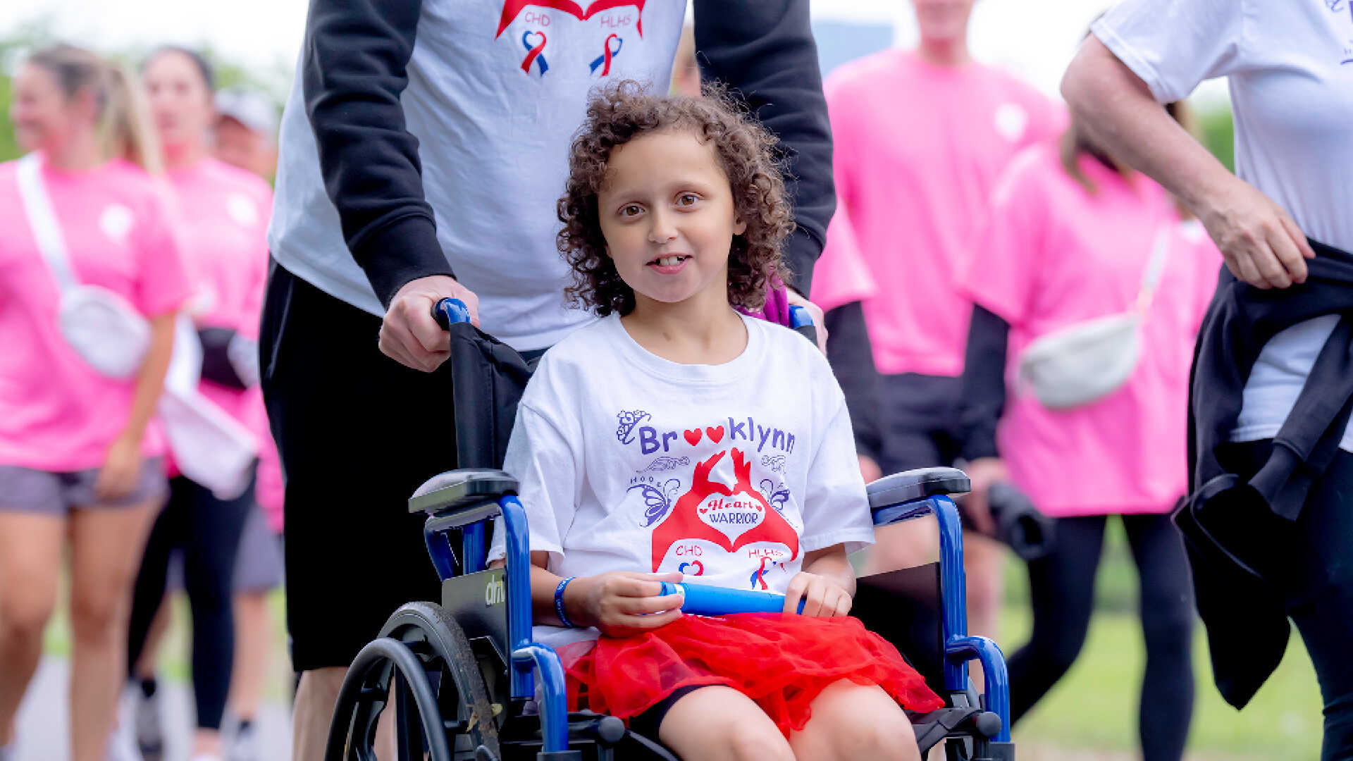 An adult pushes a young girl in a wheelchair at the Eversource Walk for Kids