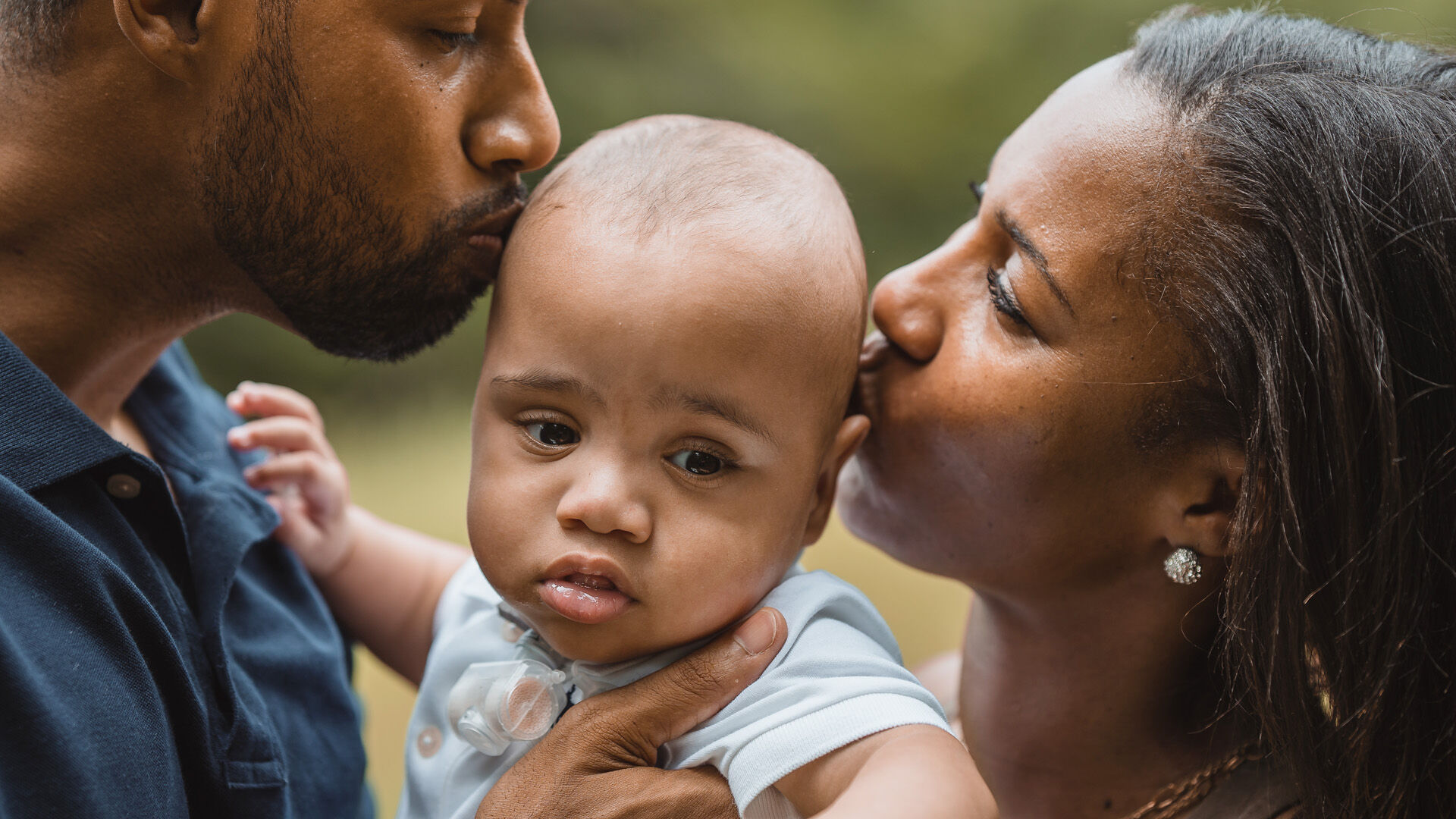 Kole being held between his mother and father as they kiss his head