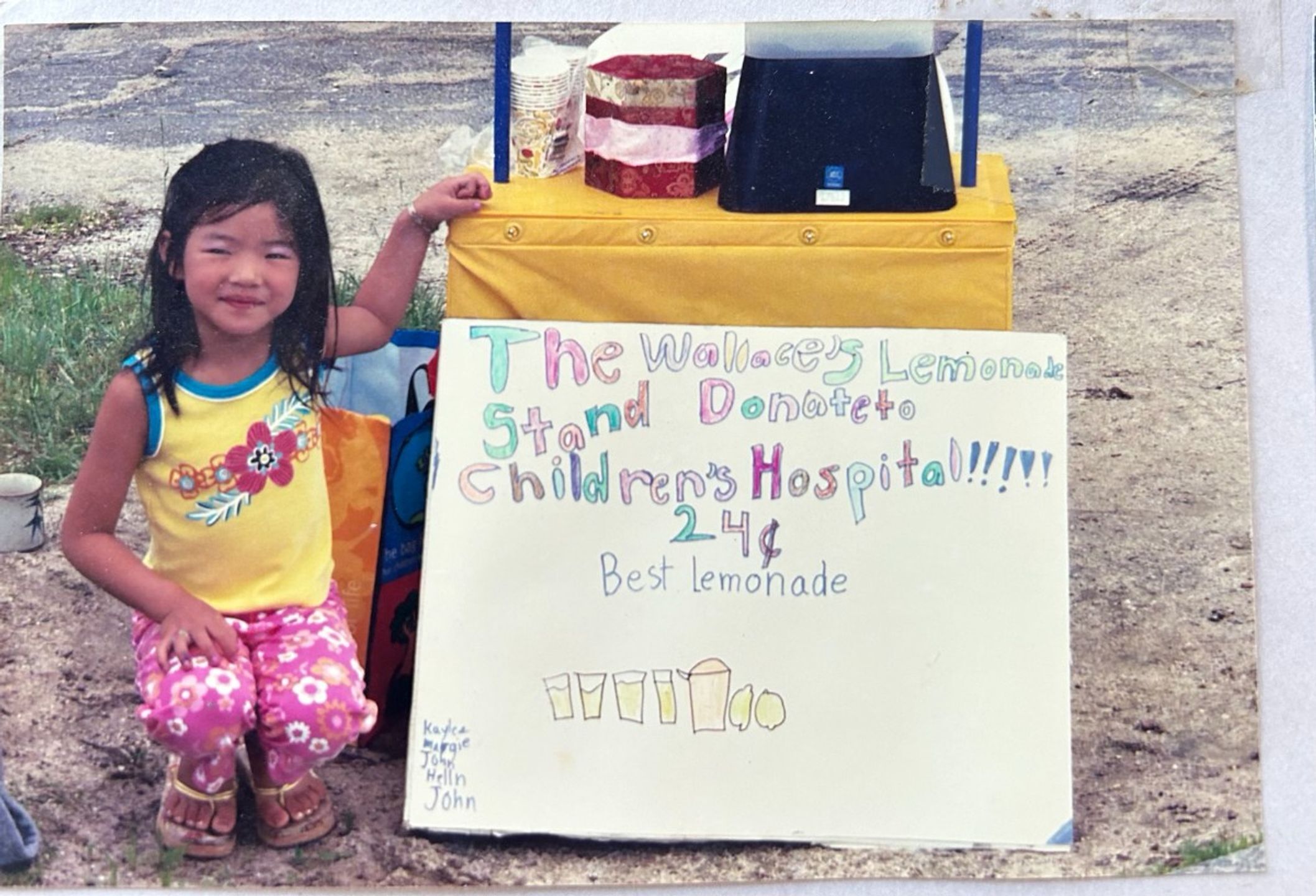 girl kneeling next to lemonade stand with homemade sign