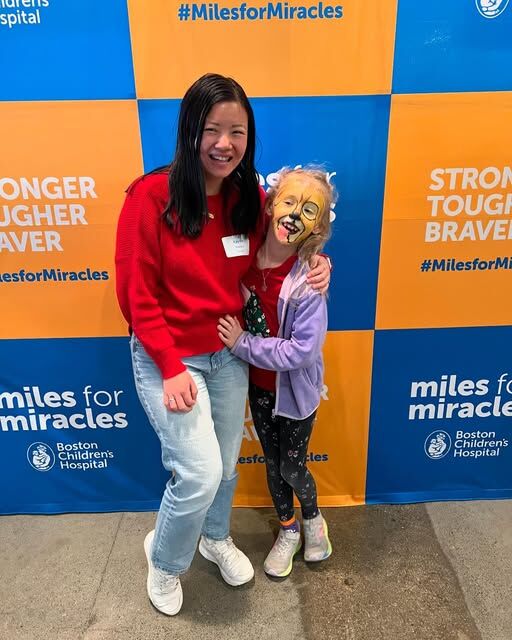 a girl standing with younger girl in front of Miles for Miracles banner