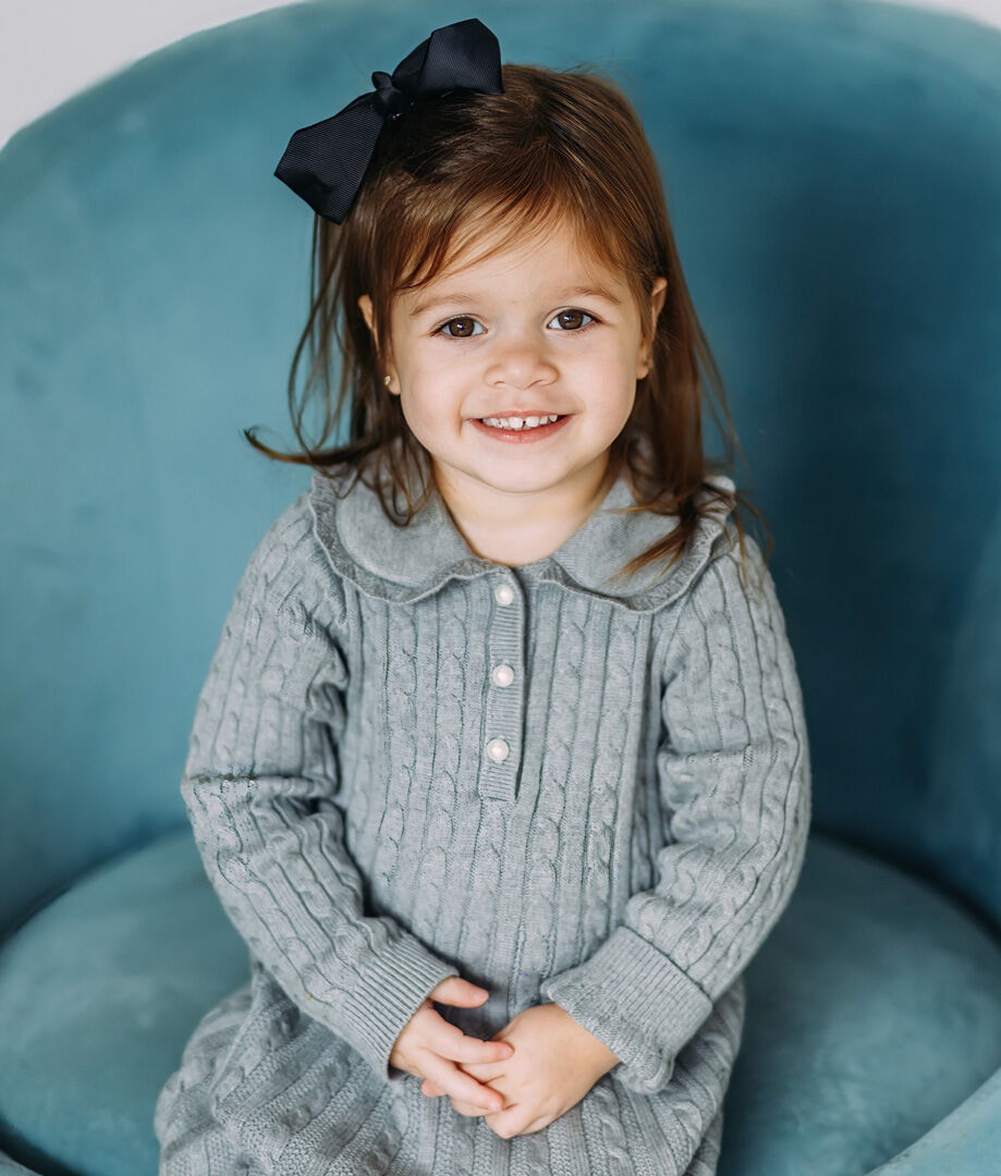 little girl with black bow in hair sitting on a blue chair
