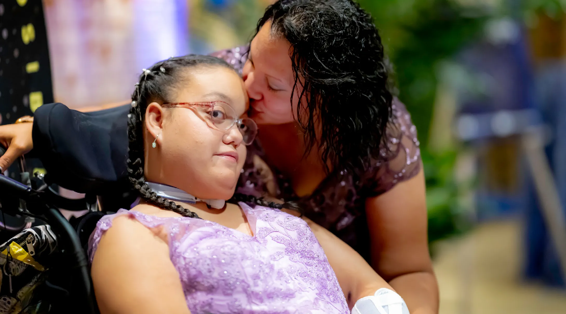 A woman kisses a girl sitting in a wheelchair on the forehead at the Milagros para Ninos Event for BCH