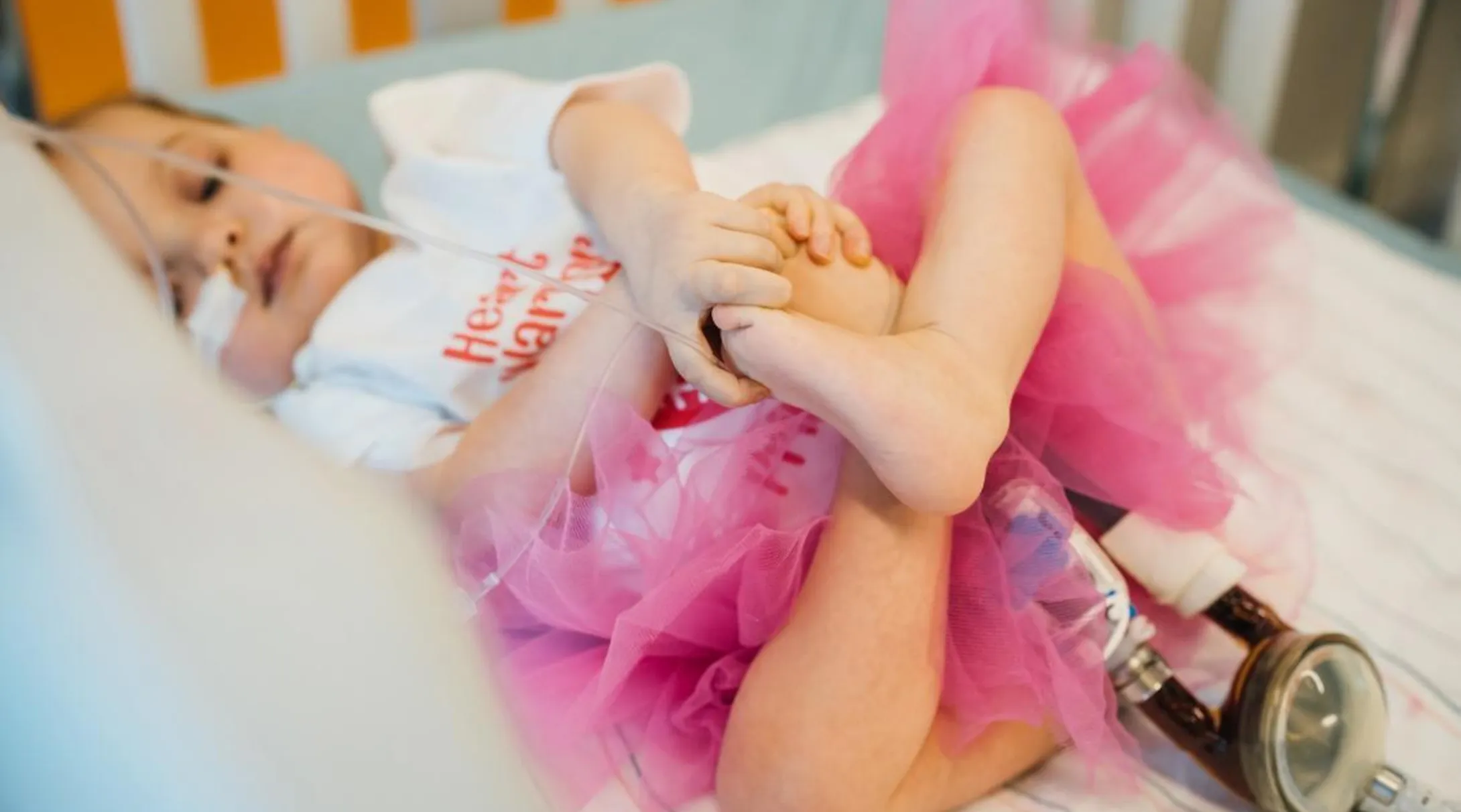 A baby with a tube coming out of her nose wearing a pink tutu and holding her feed