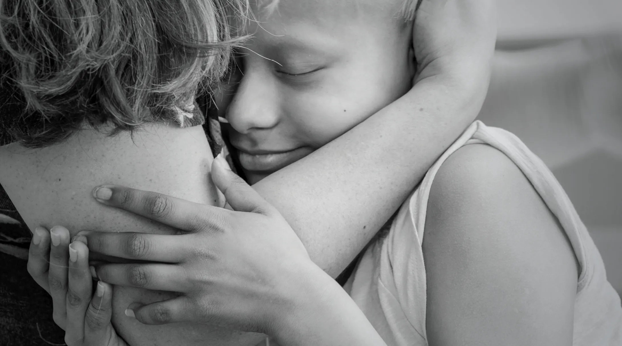 A black and white photo of a child being embraced by his mother