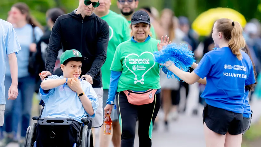 An Eversource Walk volunteer cheers on a group of event participants, one of whom is a patient in a wheelchair