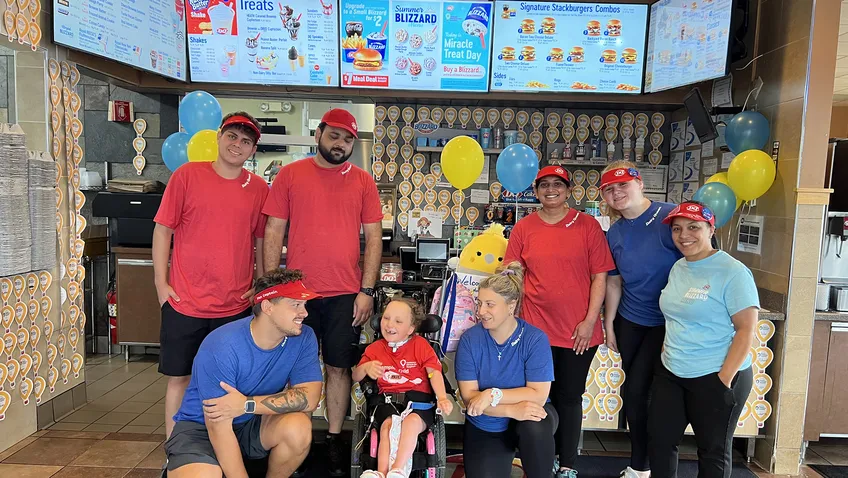 group of people surrounding young child in wheelchair inside Dairy Queen counter