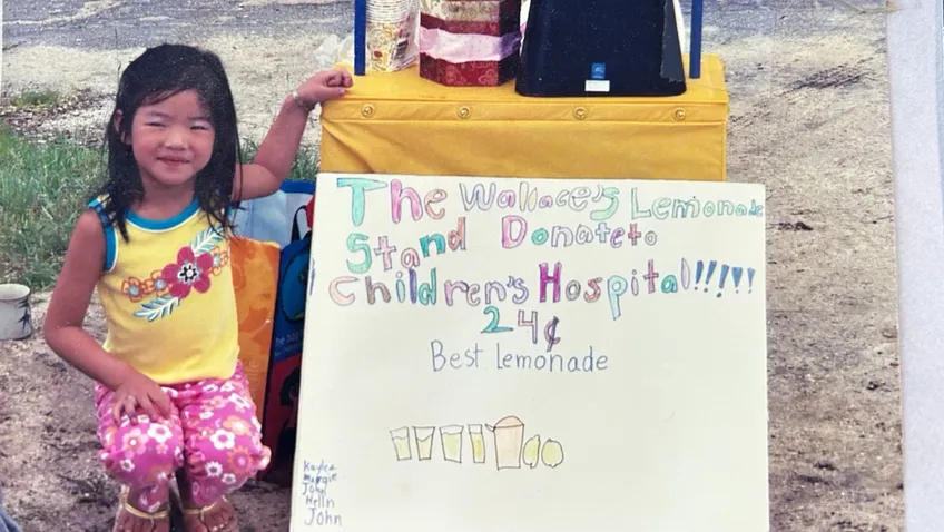girl kneeling next to lemonade stand with homemade sign