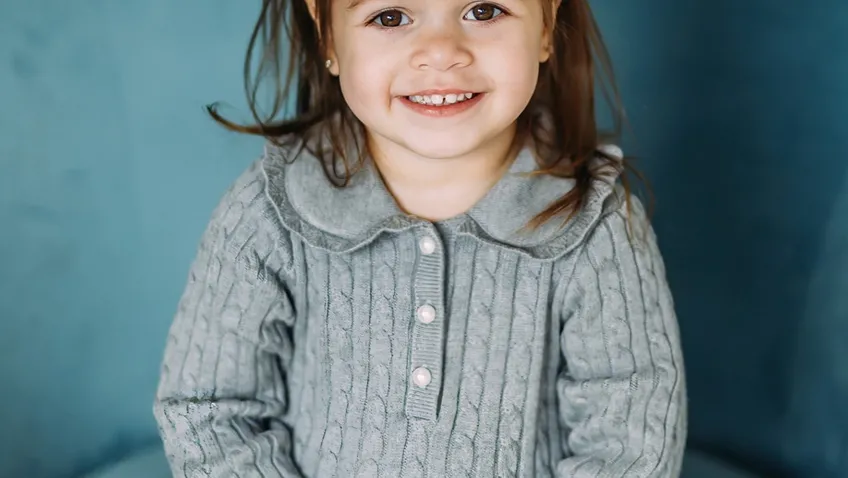 little girl with black bow in hair sitting on a blue chair