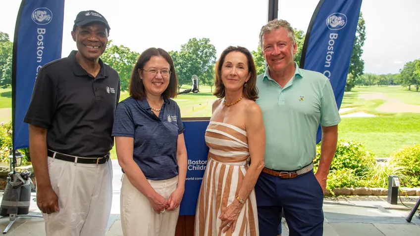 A group of four adults stand in front of a lush green golf course. They are flanked by Boston Children's Hospital banners.
