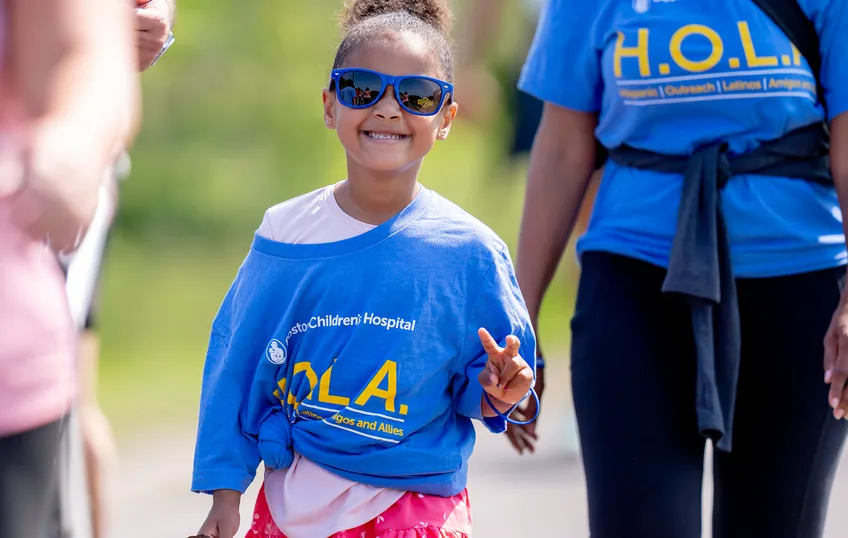 A young girl wearing sunglasses walks next to her mom at the Eversource Walk for Kids